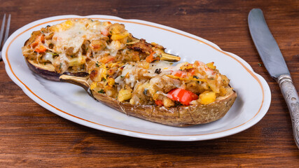 Eggplant baked with vegetables and cheese on an oval plate on a wooden table with cutlery