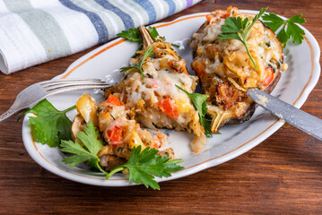 Baked eggplant with vegetables and cheese sprinkled with chopped parsley on an oval plate on a wooden table with a fork and knife, close-up