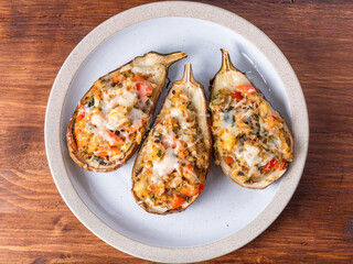 Eggplant baked with vegetables and cheese on a plate on a wooden table, close-up, top view
