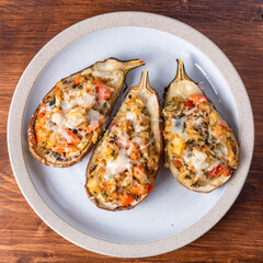 Eggplant baked with vegetables and cheese on a plate on a wooden table, close-up, top view
