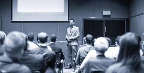 Speaker giving a talk in conference hall at business meeting event. Rear view of unrecognizable people in audience at the conference hall. Business and entrepreneurship concept.