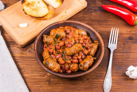 Traditional country texas cowboy dish, beef sausages with beans, onions in tomato sauce in a rustic clay plate on a wooden table, top view
