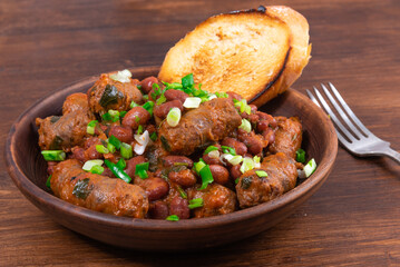 Traditional country Texas cowboy dish, beef sausages with beans in tomato sauce in a rustic clay plate with toast on a wooden table, close-up