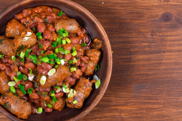 Traditional country Texas cowboy dish, beef sausages with beans in tomato sauce in a rustic clay plate on a wooden table, copy space