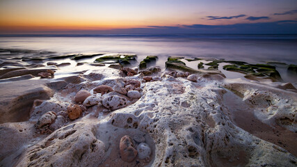 Calm ocean long exposure. Stones in mysterious mist of the sea waves. Concept of nature background. Sunset time on the beach. Sunlight on horizon. Balangan beach, Bali, Indonesia.