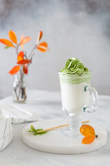 Dalgona matcha latte tea, bamboo whisk and matcha powder on a marble tray. Side view, vertical. Green matcha tea recipe, vegan menu, detox, super foods.