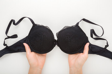 Young adult woman hands holding black bra on light gray table background. Daily underwear. Closeup. Point of view shot. Top down view. - obrazy, fototapety, plakaty