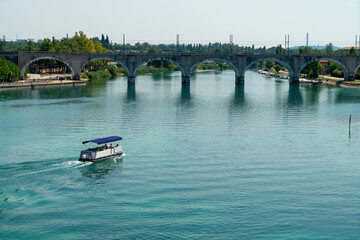 The tourist boat and the railway bridge over the Mincio river near Peschiera del Garda, Lago di Garda, Italy