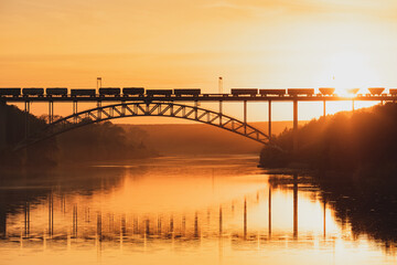 railway bridge over the river at sunset, a train is moving across the bridge