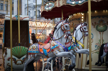 Horses with a carriage on a two-story city carousel against the backdrop of evening lights