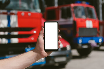 Mock up of a smartphone in the hand of a man. Against the background of fire trucks.