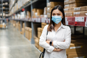 Fototapeta na wymiar woman wearing medical mask with arms crossed in warehouse store during coronavirus (covid-19) pandemic.