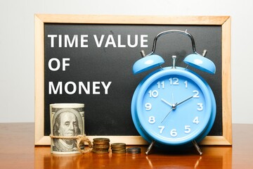 A picture of alarm clock, fake cash, coins and blackboard with time value of money word on table. 1...