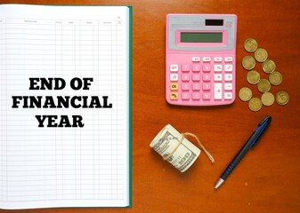 Flatlay picture of account manuscript book written End Of Financial Year with calculator, pen, fake cash and coin.