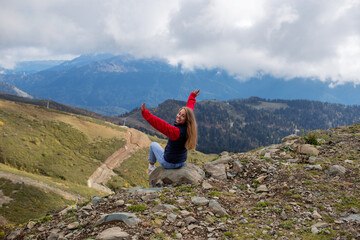 Young woman is sitting on the cliff of the mountain in Sochi, Russia.