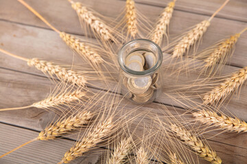 The ripe ears of wheat on the table surround a glass jar with euro coins