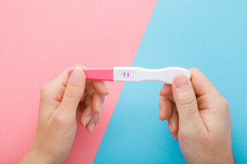 Young adult woman and man hands holding together pregnancy test with two stripes on light pink blue...