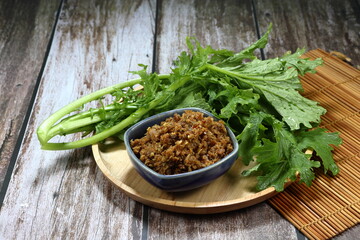 Spicy minced fish meat with chilly, shallot and local spices in small bowl serving with fresh green vegetable on the wooden plate. Famous traditional spicy paste in Asia restaurant. 