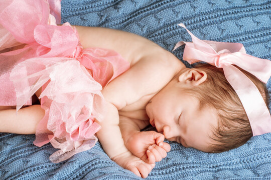 a newborn girl in pink chiffon skirt, with a bow on her head, lies on a blue blanket.
