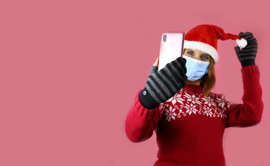 Fototapeta na wymiar A young girl in santa claus hat and medical protective mask takes a selfie on her phone camera. Congratulations during self-isolation, coronavirus pandemic