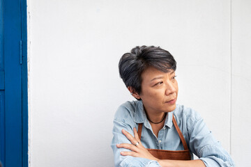 Old Asian woman Wearing an apron and planning to do housework, painting, or planing for home improvement sitting in front of the white wall. Elderly concept.