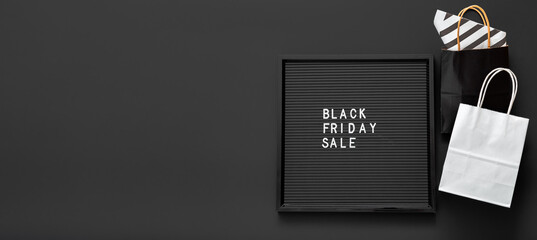 Black Friday sale text on black Letter Board with shopping paper bags on black background. Delivery mock up black and white craft paper bag package. Long web banner with copy space.