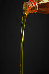 Pouring olive oil from a bottle on darck background