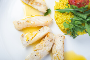 Fillet of white fish in sauce on a plate with garnish and herbs.
