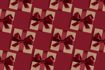 Repetitive pattern made of gift boxes tied with ribbons on a red background. Holidays concept.