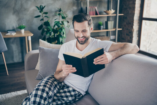 Photo of domestic homey handsome guy stay home quarantine time reader book worm good mood sit comfy cozy sofa modern interior flat living room apartments indoors
