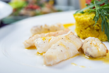 Fillet of white fish in sauce on a plate with garnish and herbs.