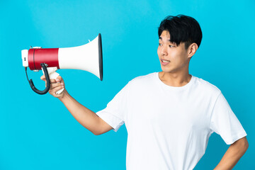 Young Chinese man isolated on blue background holding a megaphone with stressed expression