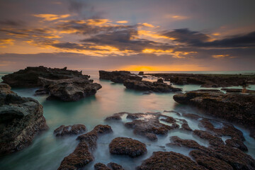 Beautiful seascape. Long exposure rocky beach during low tide. Panoramic ocean view. Composition of nature. Sunset scenery background. Cloudy sky. Water reflection. Mengening beach, Bali