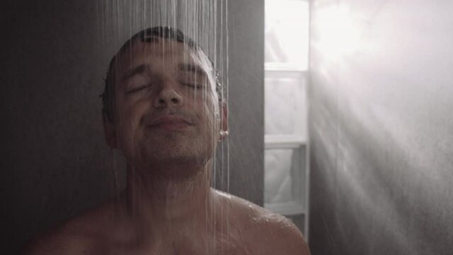 Close-up shot a middle-aged caucasian man standing under the shower and getting relaxed with cool water, then he coming up to the camera with relieved look