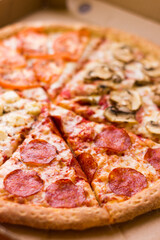 Close up fresh hot pizza with salami lies in a cardboard box by the window. Salami pizza, tomato mushrooms and cheese taste