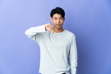 Obraz premium Young Chinese man isolated on purple background showing thumb down with negative expression