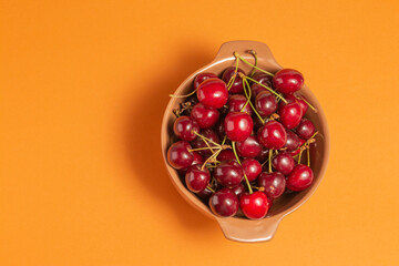 Cherries with water drops in clay bowl on terracota background. Fruit bowl. Top view. Delicious food. Copy space. High quality closeup photo.
