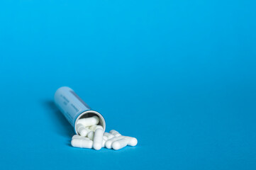 A bottle with a bunch of white capsules of tablets on a blue background.