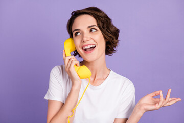 Portrait photo of sociable smiling girl keeping retro telephone yellow handset talking isolated on vivid purple color background