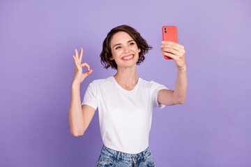 Photo portrait of happy female blogger taking selfie smiling showing okay gesture with fingers isolated on bright purple color background