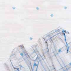 White cotton pajamas with blue checks or stripes, on white wooden background. Nightwear for sleeping with snowflakes for winter time.