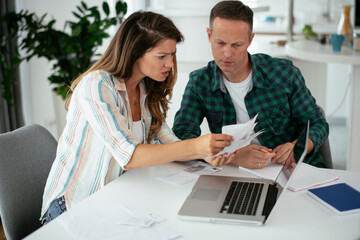 Husband and wife preparing bills to pay. Young couple using laptop.