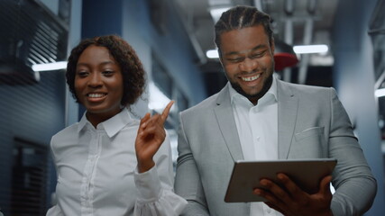 Positive afro business couple discussing plan on tablet computer in office