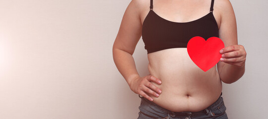Overweight fat woman showing her belly fat with paper heart, selective focus. Bodysitive concept