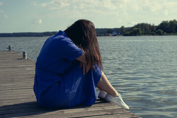 Sadness Woman Sitting by the River on pier. Empty place for text. Bad Day Concept.