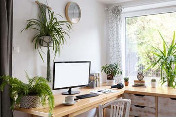Modern office desk in creative room interior at home with blank monitor screen of computer, plant, clock, chair and window. Workplace during home office. Business and work online. Mock up.