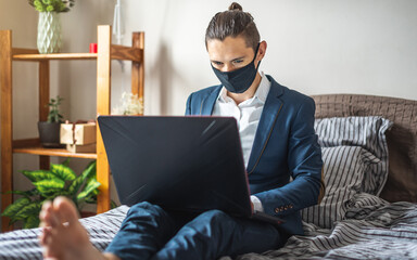 Businessman man in a suit is working remotely on a laptop in bed at home. Adapting to work during a pandemic