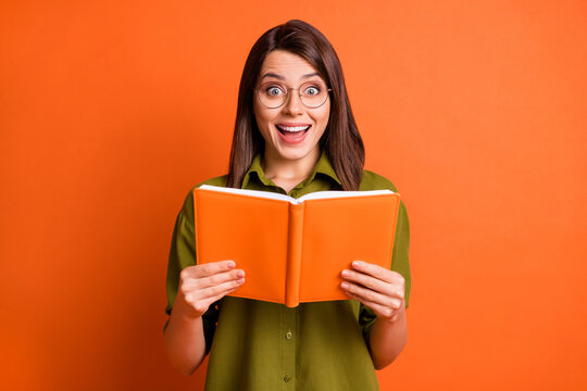 Photo portrait of surprised brunette girl keeping book laughing isolated on vivid orange color background