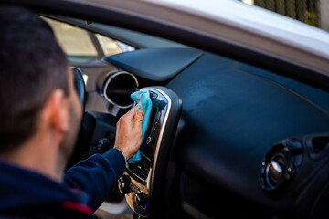 The young man is just finishing washing the car. He wipes the plastic parts of the car's interior with a blue cloth.