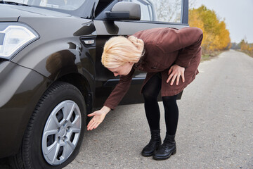 Fototapeta na wymiar A young blonde woman stands near her car with a flat tire.